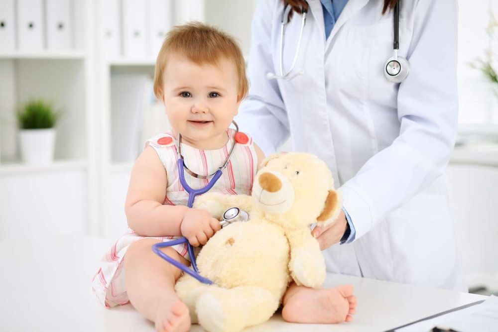 Baby sitzt mit einem Stofftier neben einer Ärztin